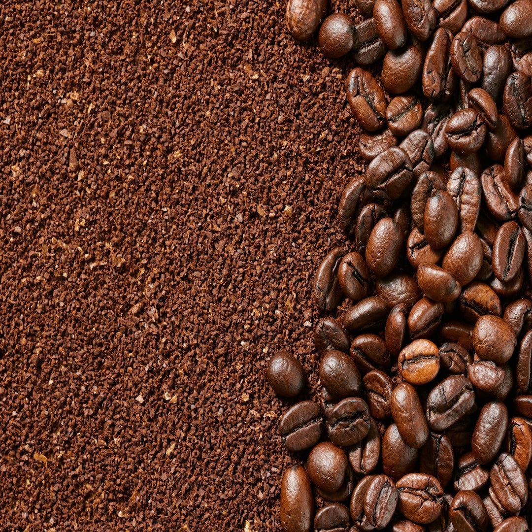 Close-up of roasted coffee beans and ground grains used in natural skincare products, highlighting the antioxidant and circulation-boosting benefits of coffee essential oil.